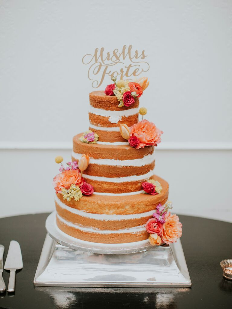 three tier vanilla sponge naked wedding cake on silver stand decorated with pink and orange flowers and gold mr & mrs. cake topper