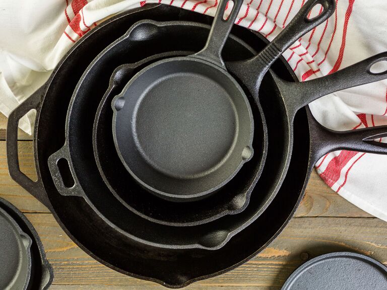 cast iron pans stacked on wood table next to dish towel