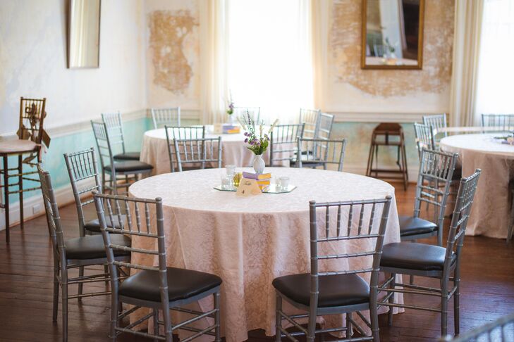 Tables at the reception were covered with pretty blush tablecloths and arranged with silver chiavari chairs. Centerpieces consisted of an assortment of wildflowers in milk glass vases on a stack of lavender books.
