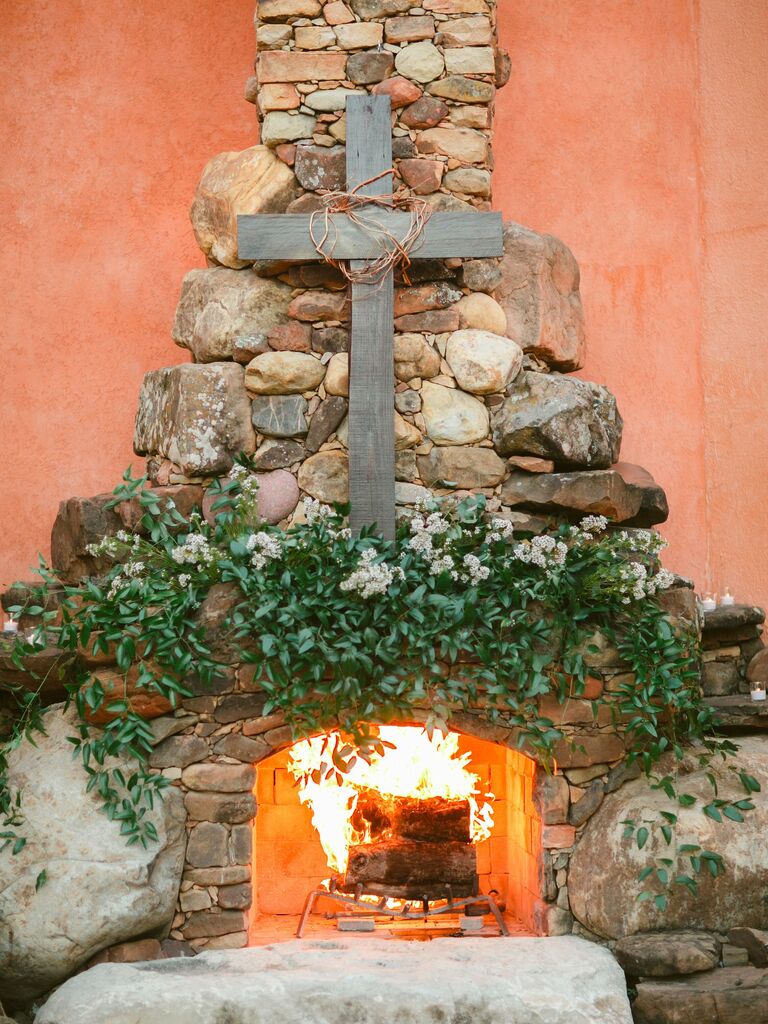 simple wedding fireplace decor idea with wooden cross and greenery on stone hearth