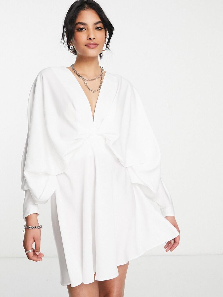Model wears a flowy mini dress with long sleeves. 