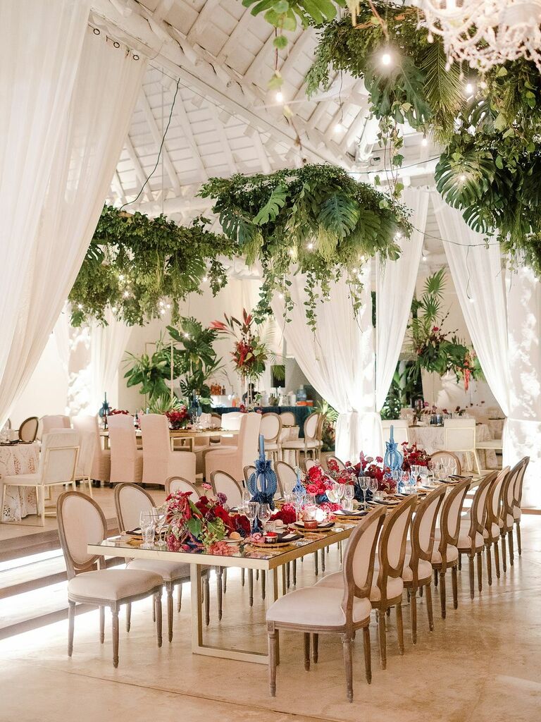 indoor wedding reception with tropical monstera leaves hanging above long wooden banquet table
