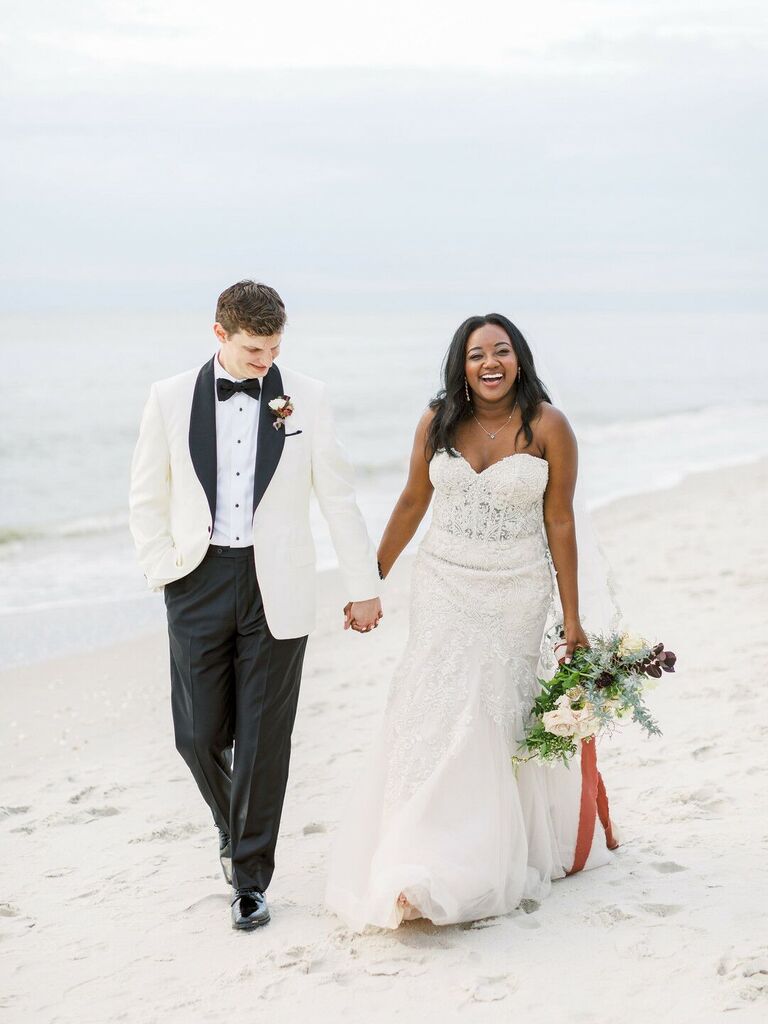 Couple walk hand in hand at a beach wedding. 
