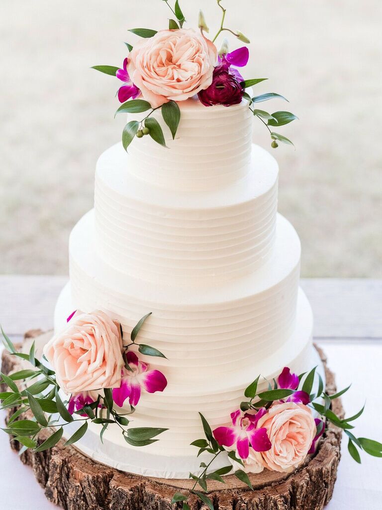 four tier buttercream wedding cake with pink roses, fuchsia orchids and greenery displayed on wooden tree cake stand