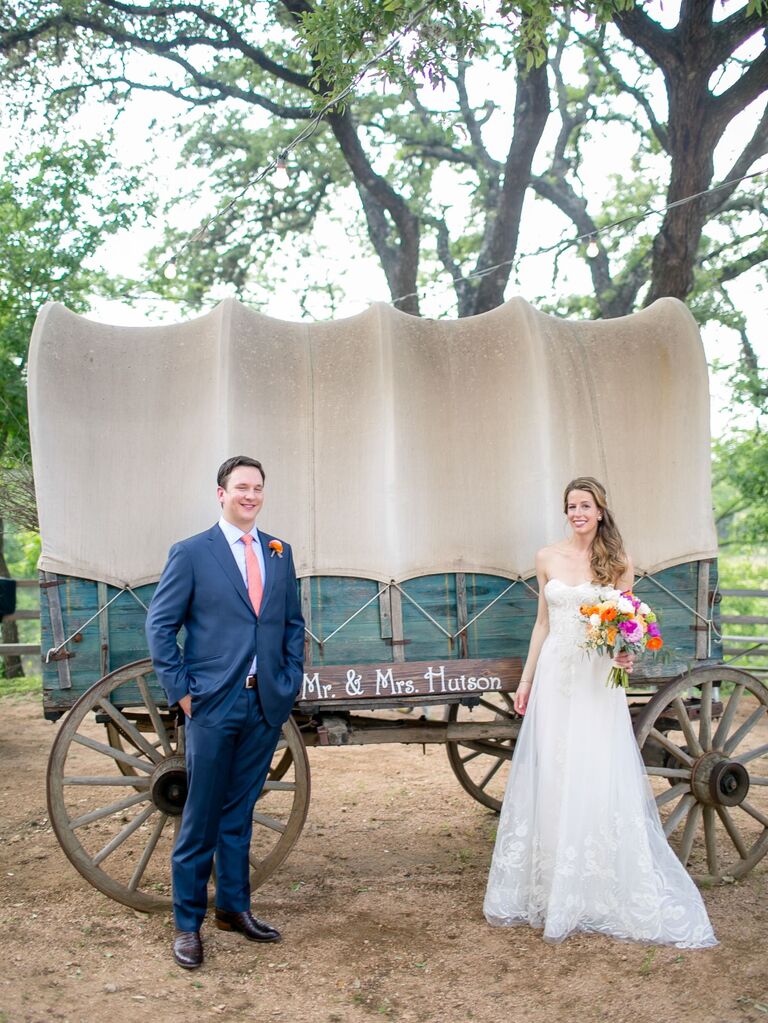 Newlyweds smile and pose in front of a covered horse carriage. 