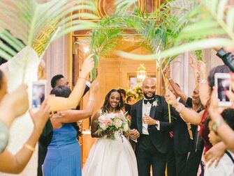 Couple enters their reception while guests wave tropical palm leaf fronds. 