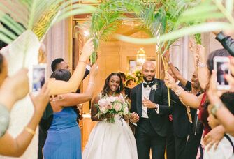 Couple enters their reception while guests wave tropical palm leaf fronds. 