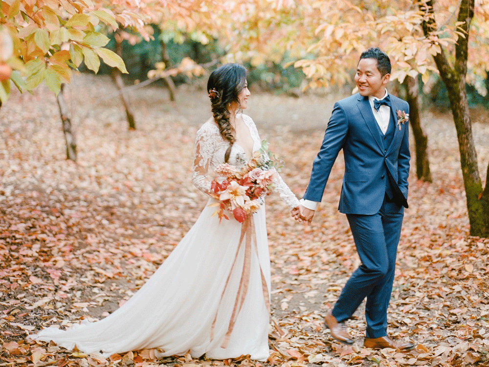Couple strolling through autumn leaves at their fall wedding