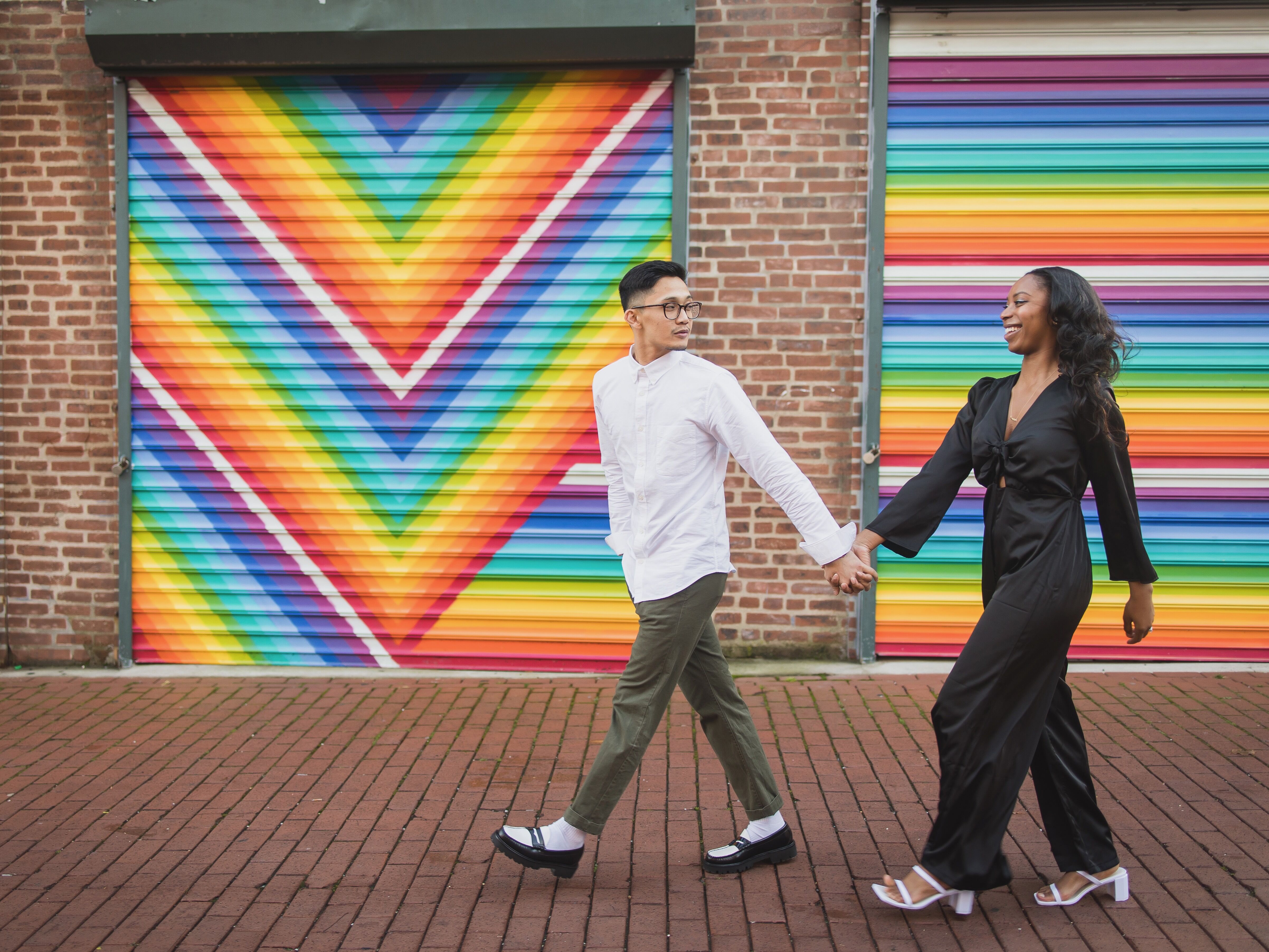 couple holding hands and walking in front of colorful mural for engagement photo shoot 