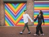 couple holding hands and walking in front of colorful mural for engagement photo shoot 