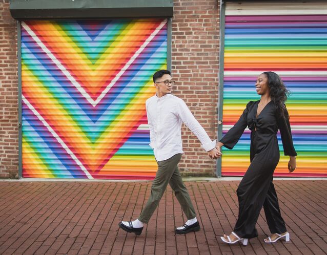 couple holding hands and walking in front of colorful mural for engagement photo shoot 