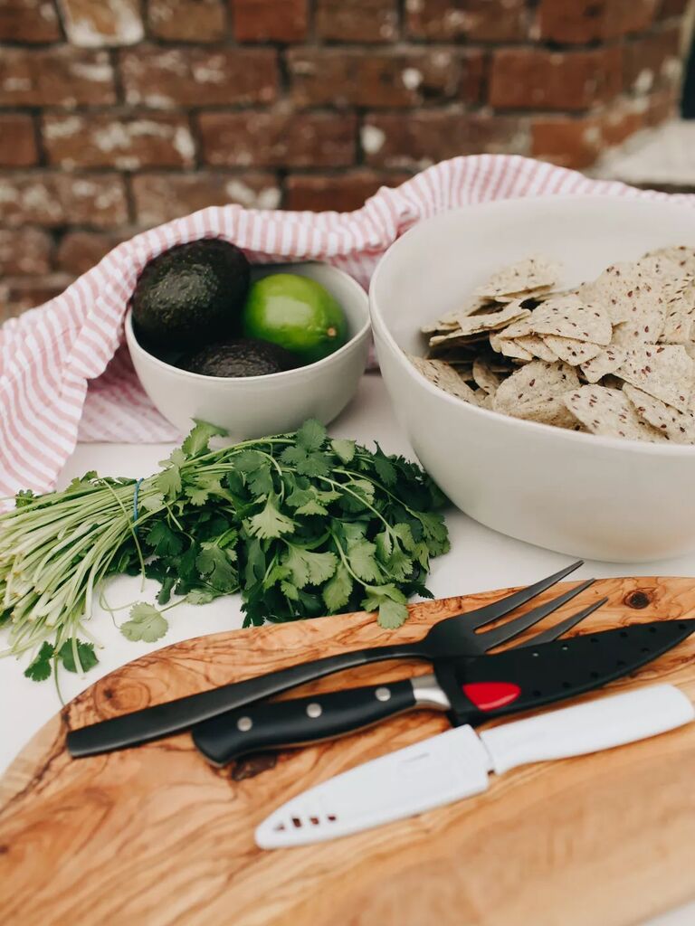 A guacamole station features avocados, limes, cilantro, tortilla chips and a cutting board. 
