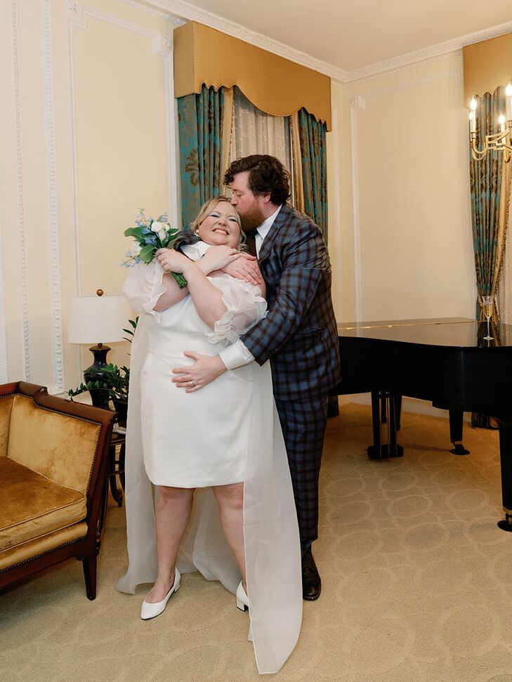 Groom in Blue Plaid Suit Hugs and Kisses Bride in Minidress and Bouquet