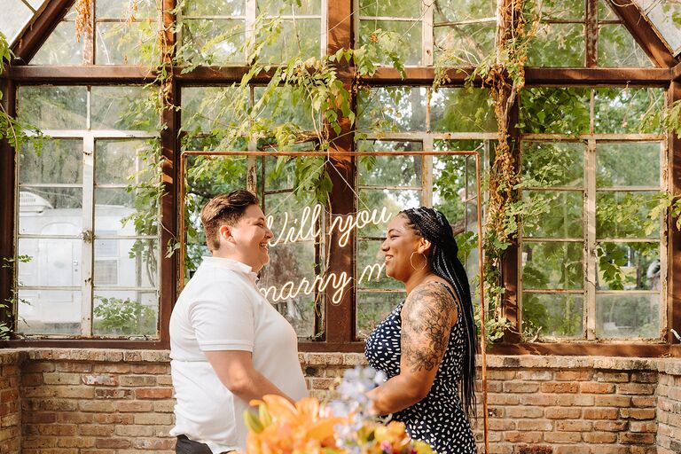 couple proposing in front of neon will you marry me sign