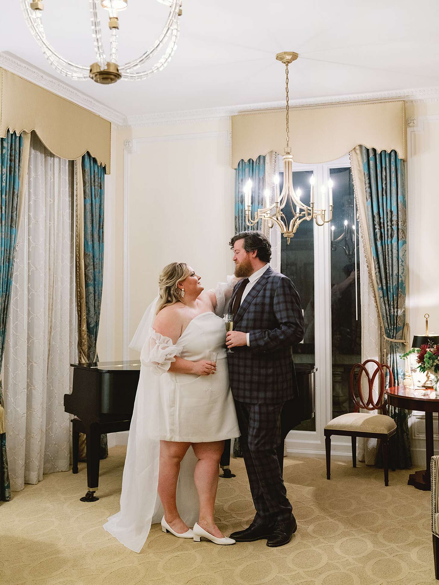 Bride in a Minidress and Groom in Checkered Suit With Champagne in Hotel  Suite
