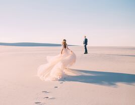 Bride in wedding dress running to husband in sandy desert