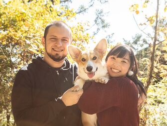 A couple smile, on a walk in the woods with their dog.