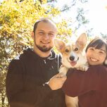 A couple smile, on a walk in the woods with their dog.