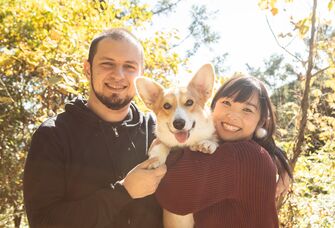 A couple smile, on a walk in the woods with their dog.