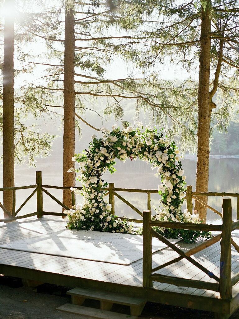 Lush white floral ceremony arch at outdoor lakeside wedding