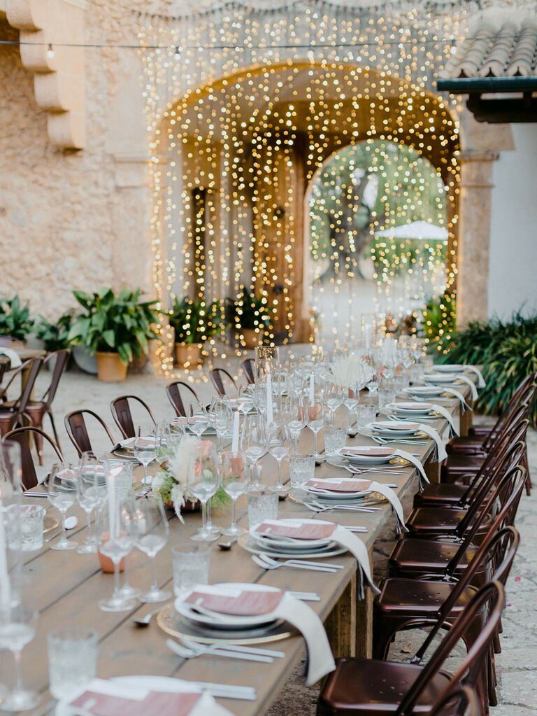 Outdoor wedding reception tables with curtain string lights hanging from arch