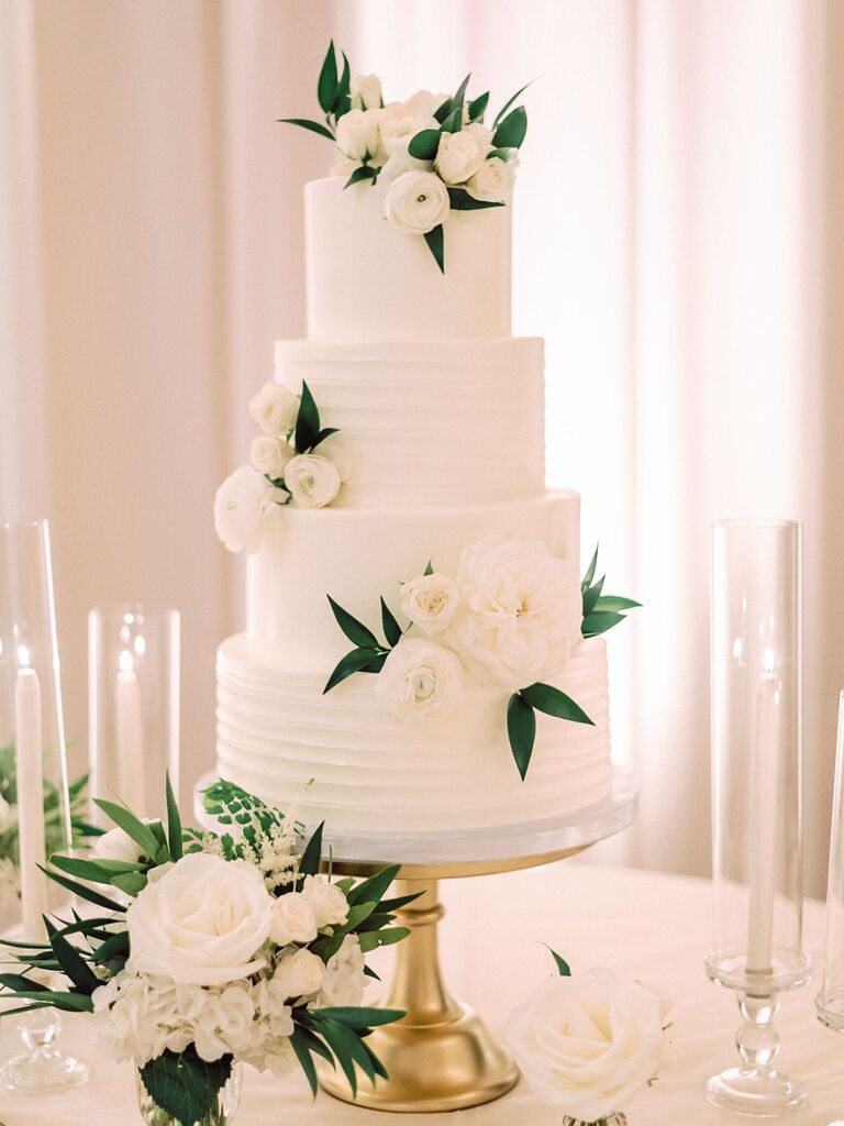four tier white buttercream wedding cake with white flowers and greenery