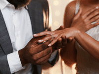 A man putting a engagement ring on a woman's finger. 