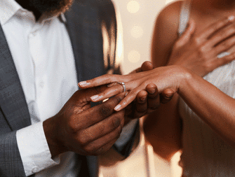 A man putting a engagement ring on a woman's finger. 