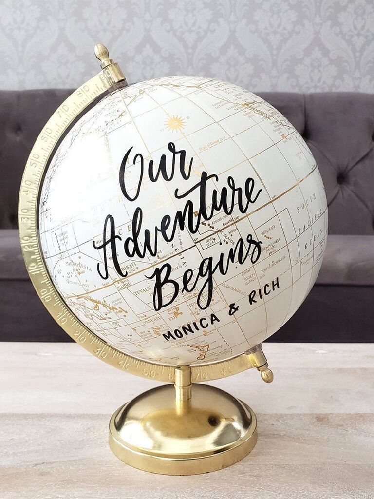 'Our Adventure Begins' and couple's names in black script on white globe with gold stand