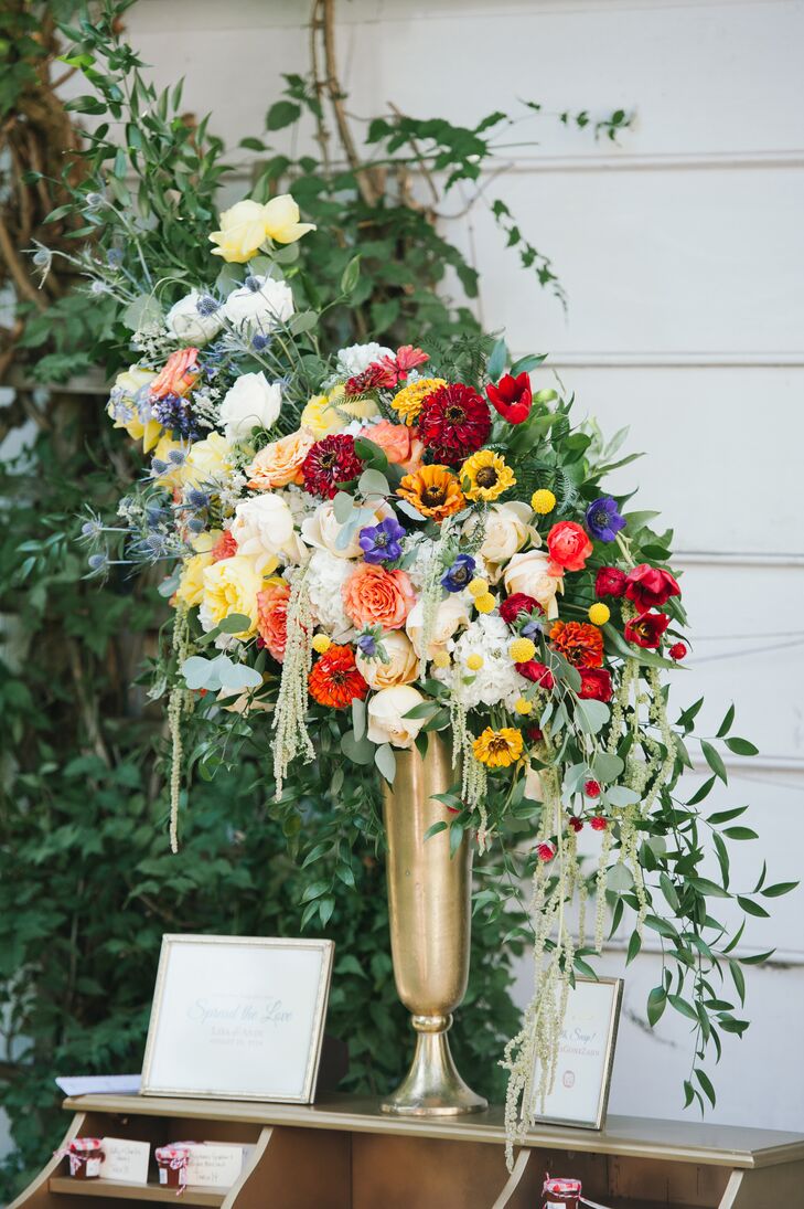 Warm colored hydrangeas, yarrows and zinnias accented with fern, seeded eucalyptus and green amaranths in a gold Milan vase were arranged by La Petite Fleur.