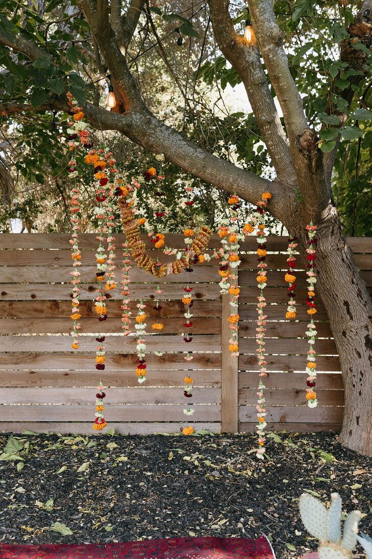 An asymmetrical ceremony backdrop at a casual motel wedding with desert-inspired colors such as deep purple, yellow, white and burnt orange on marigold and carnation flowers strung up and suspended from a tree.