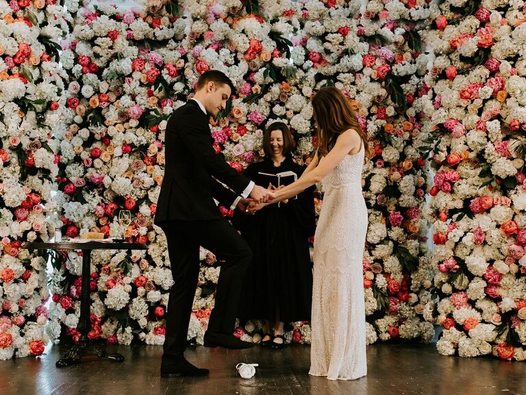 Bride and groom getting married in front of a colorful wedding flower wall.