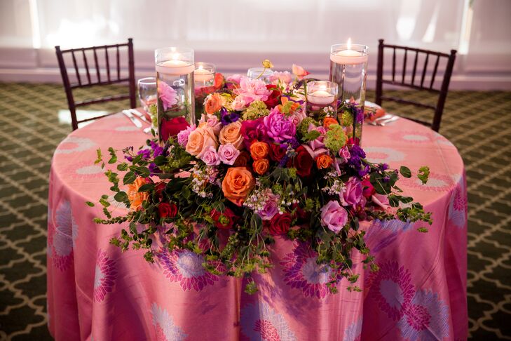 Amy and Paul's sweetheart table stood out with a number of bright blooms. Pink, orange, red and fuchsia roses were matched with greenery, baby’s breath and pink chrysanthemums for an eye-catching arrangement. Garden District-Naples also surrounded the blooms with floating tea-light candles in cylinder vases for a soft, added glow.
