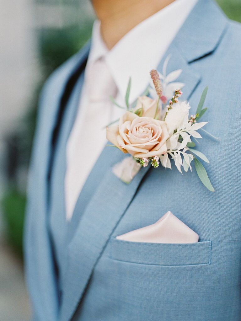 close up of pastel wedding boutonniere with pink rose and bleached greenery on light blue suit jacket