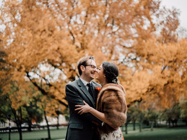 A woman and a man laugh together in front of an autumnal tree for their engagement photo
