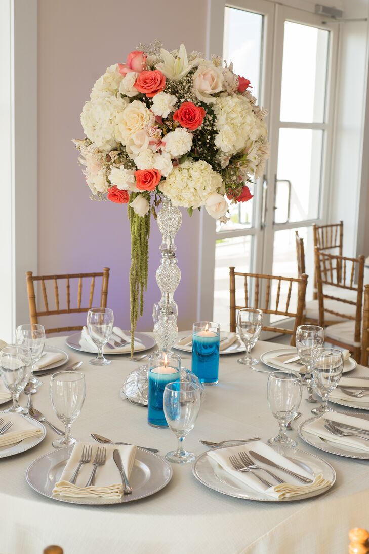 Tall flower arrangements of ivory and coral roses, hydrangeas, baby's breath and touches of hanging amaranthus, displayed in crystal vases, decorated the smaller, round dining tables. Floating candles in blue water brought in a beach-inspired touch.