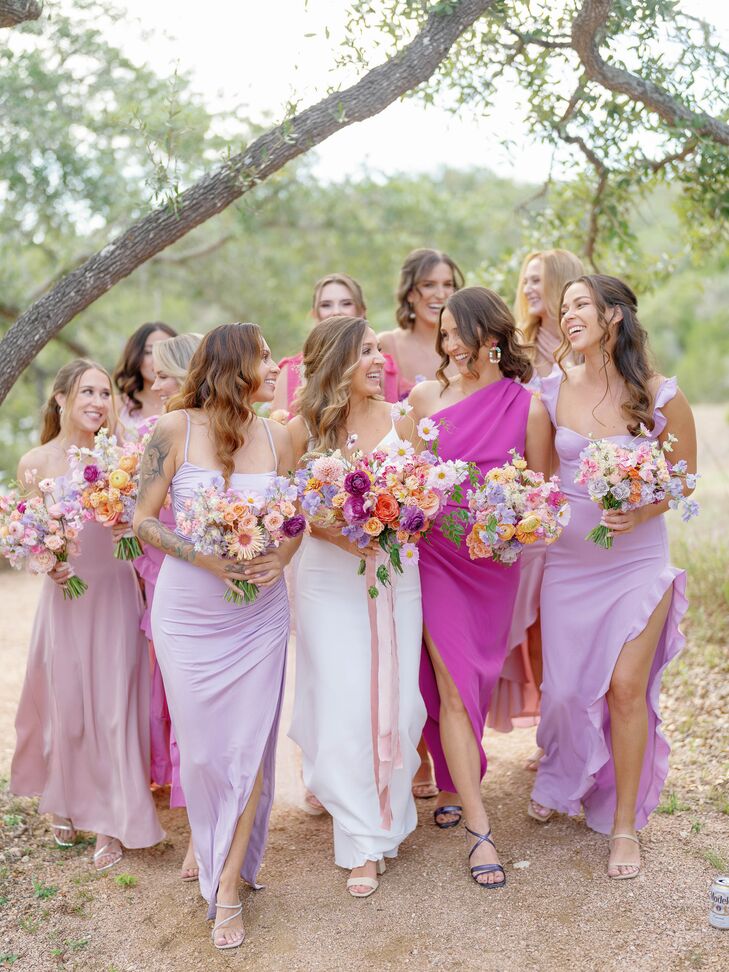 A bride in a fitted gown and a bright and pastel bouquet walking with her bridesmaids in different pastel gowns in shades of lavender, blush and purple with flowers of complementing shades.