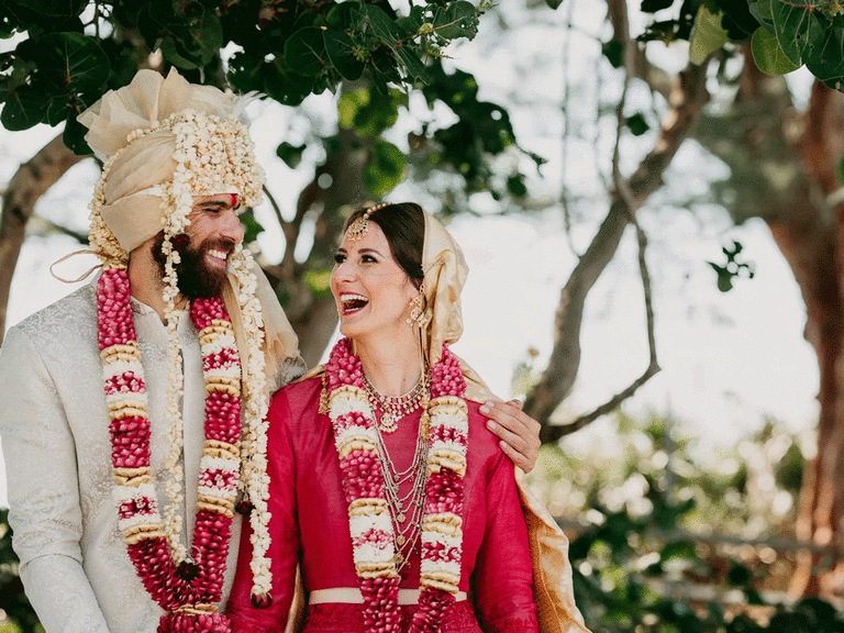Bride and groom smiling while wearing traditional Indian wedding attire.
