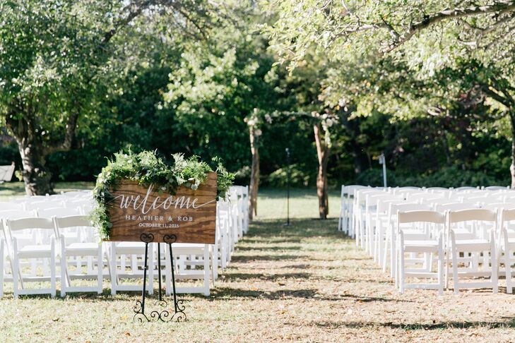 Lush greenery lined the wooden welcome sign, provided by Belovely. Romantic white folding chairs were situated in an apple orchard for the ceremony.