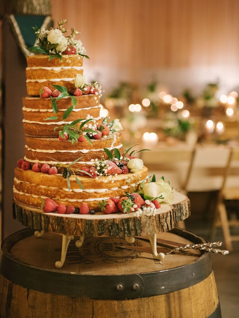 naked wedding cake on top of wooden wine barrel with tiers aligned to the left and decorated with fresh fruit