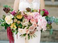 bride holding oversized wedding bouquet with pale pink roses, peonies, yellow roses, and eucalyptus