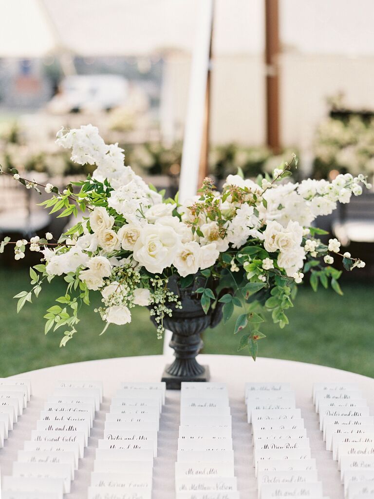 wedding escort card display with white and greenery centerpiece in black urn vase
