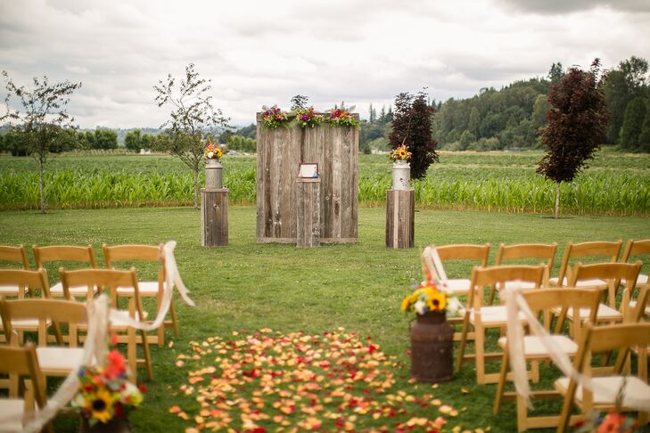 The couple was married at an altar surrounded by wood pillars and rustic wood panel backdrop at Craven Farm in Snohomish, Washington. The aisle was decorated with wildflower arrangements, drapery and colorful petals.
