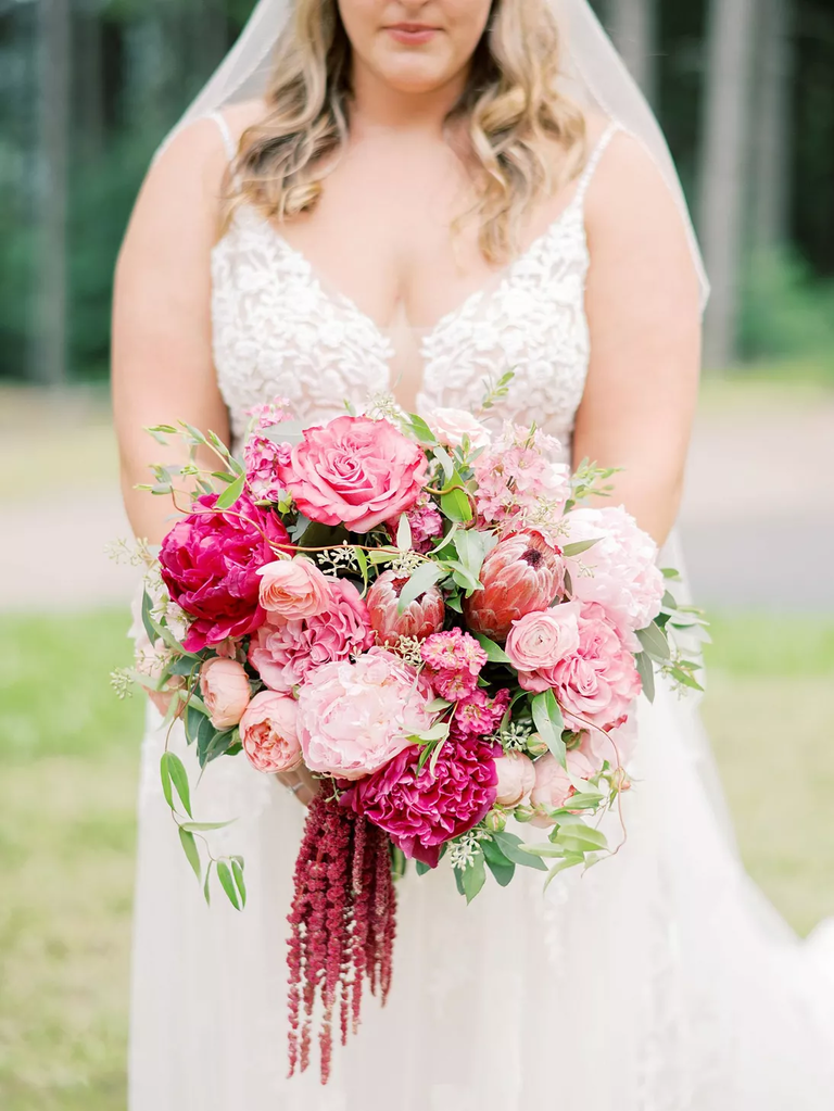 A bride stands holding an ombré bouquet in different shades of pink.