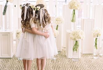 Two flower girls hug in a chic reception space. 