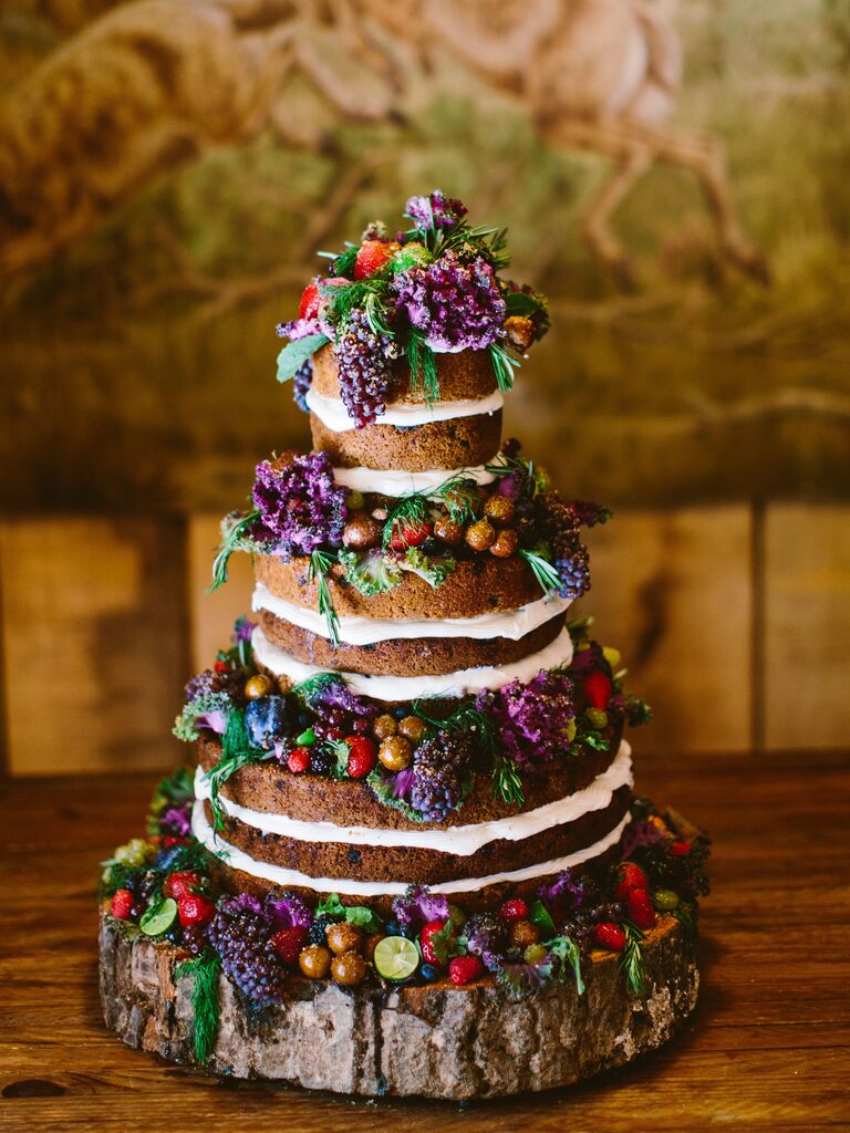 three tier naked wedding cake decorated with purple grape bunches, greenery, strawberries and purple cabbage leaves on top of wooden cake stand