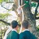 Grooms Embrace and Watch Aerial Silk Performer Hanging Off of a Tree