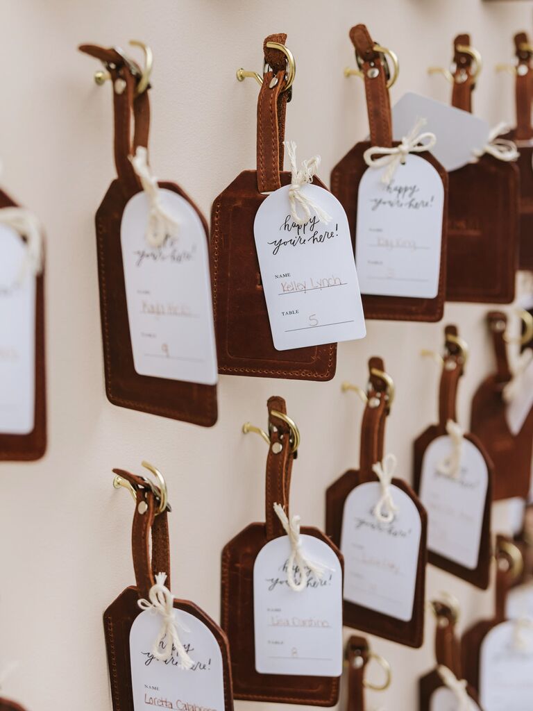 creative wedding escort card idea row of brown leather luggage tags hanging from gold hooks on wooden board