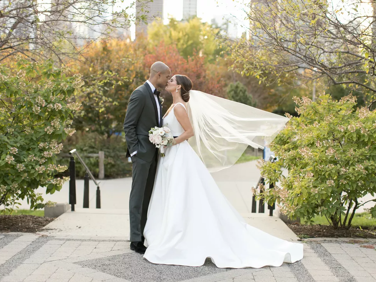 A couple leans in for a kiss among the greenery at their favorite park.
