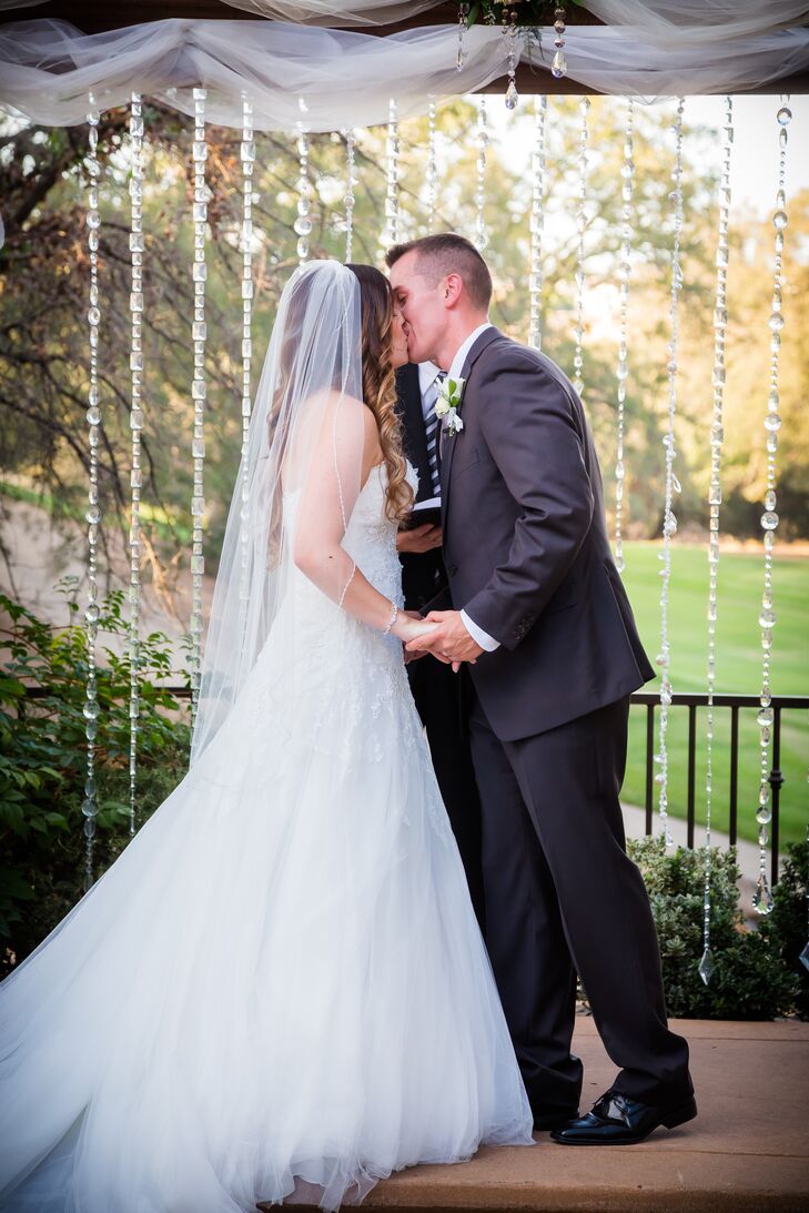 Marisa and Mikhail shared their first kiss at the wedding arch that was draped with strings of crystals and covered with white linens. Marisa wore a traditional ivory veil made of tulle on the day of the wedding, which went nicely with her ivory Pronovias dress.